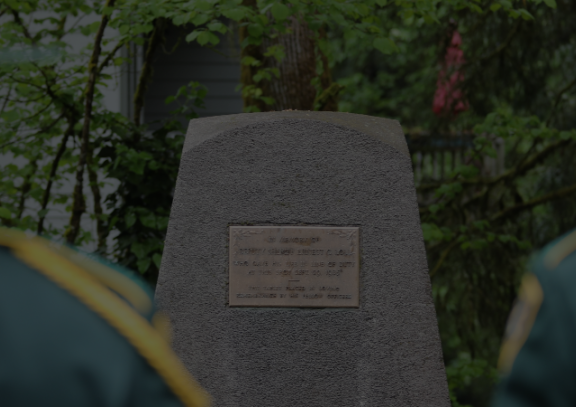 Backs of two Honor Guard members in the foreground with Loll Memorial stone in the background.