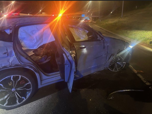 A white BMW shown with extensive damage after crashing on the freeway at night. 