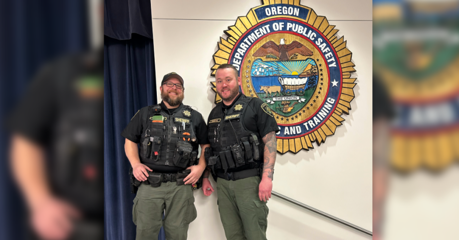 Gun Dispossession Unit Deputies Sullivan and Robbins stand before a Department of Public Safety and Standards Training emblem after presenting on the topic of Extreme Risk Protection Orders, or ERPOs.