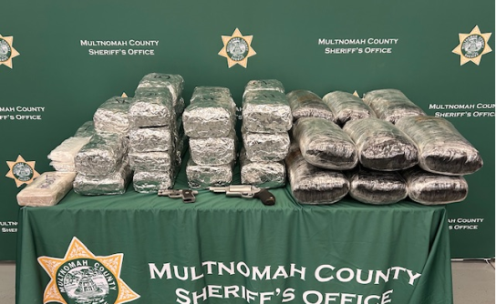Large amount of illegal narcotics wrapped in plastic on a table with two firearms. Green background with Multnomah County Sheriff's Office logo.