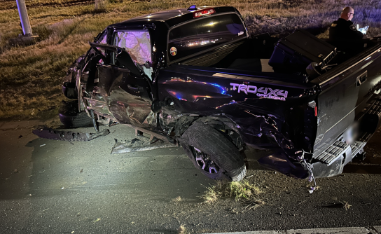 A black pickup truck is shown on the freeway at night crashed after rolling over. 