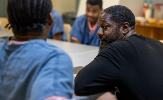 Nathanyel Israel sits at a table alongside adults in custody enrolled in his ManUp Program.